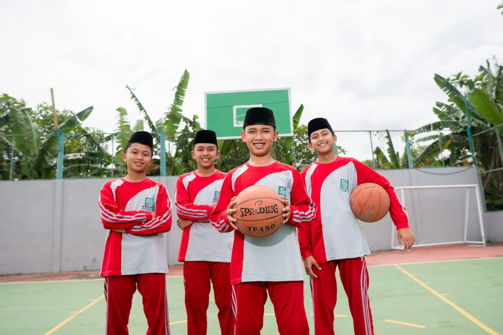 Empat santri putra berpose dengan bola basket di lapangan.