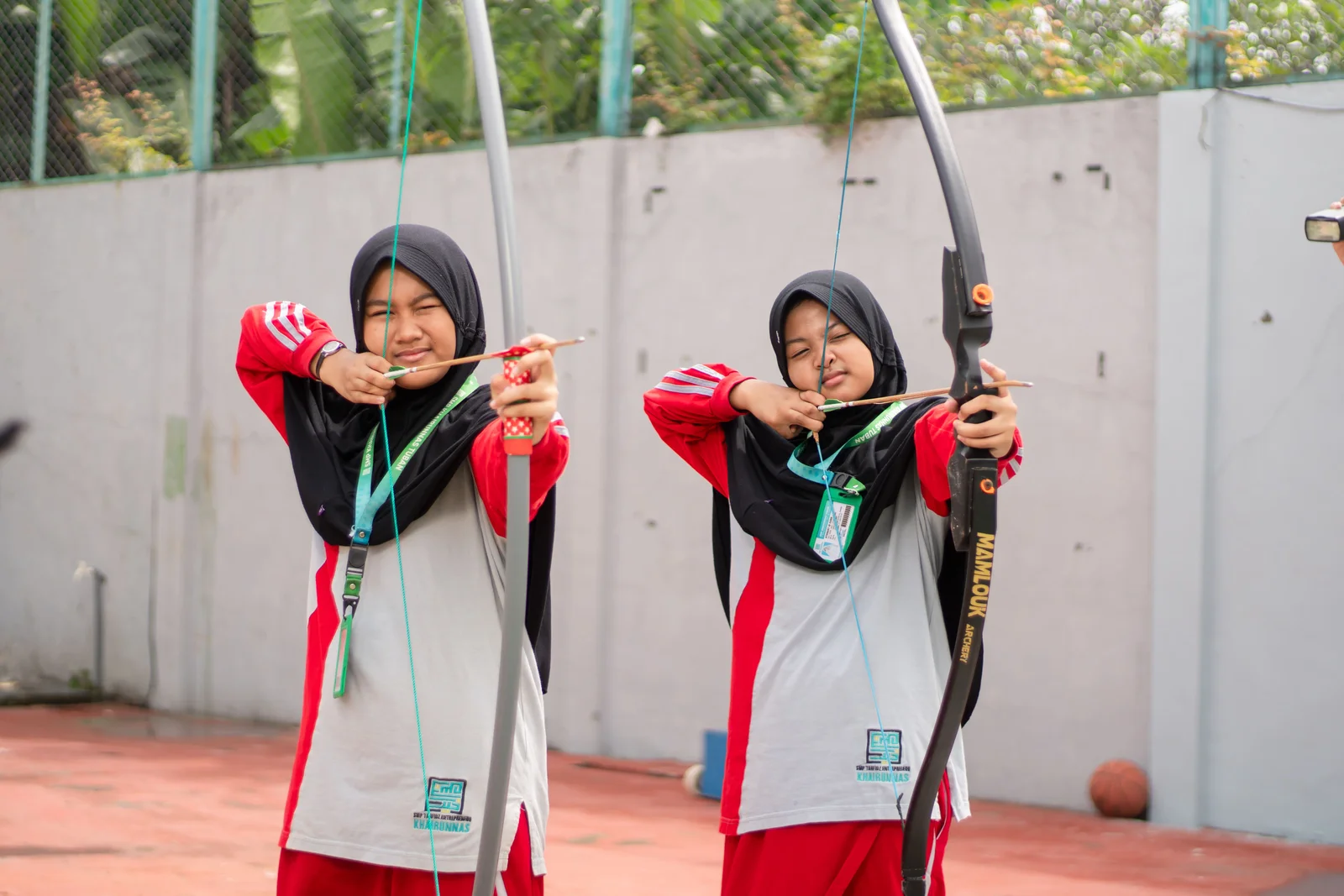 Dua santriwati membidik dengan busur dan anak panah di lapangan.