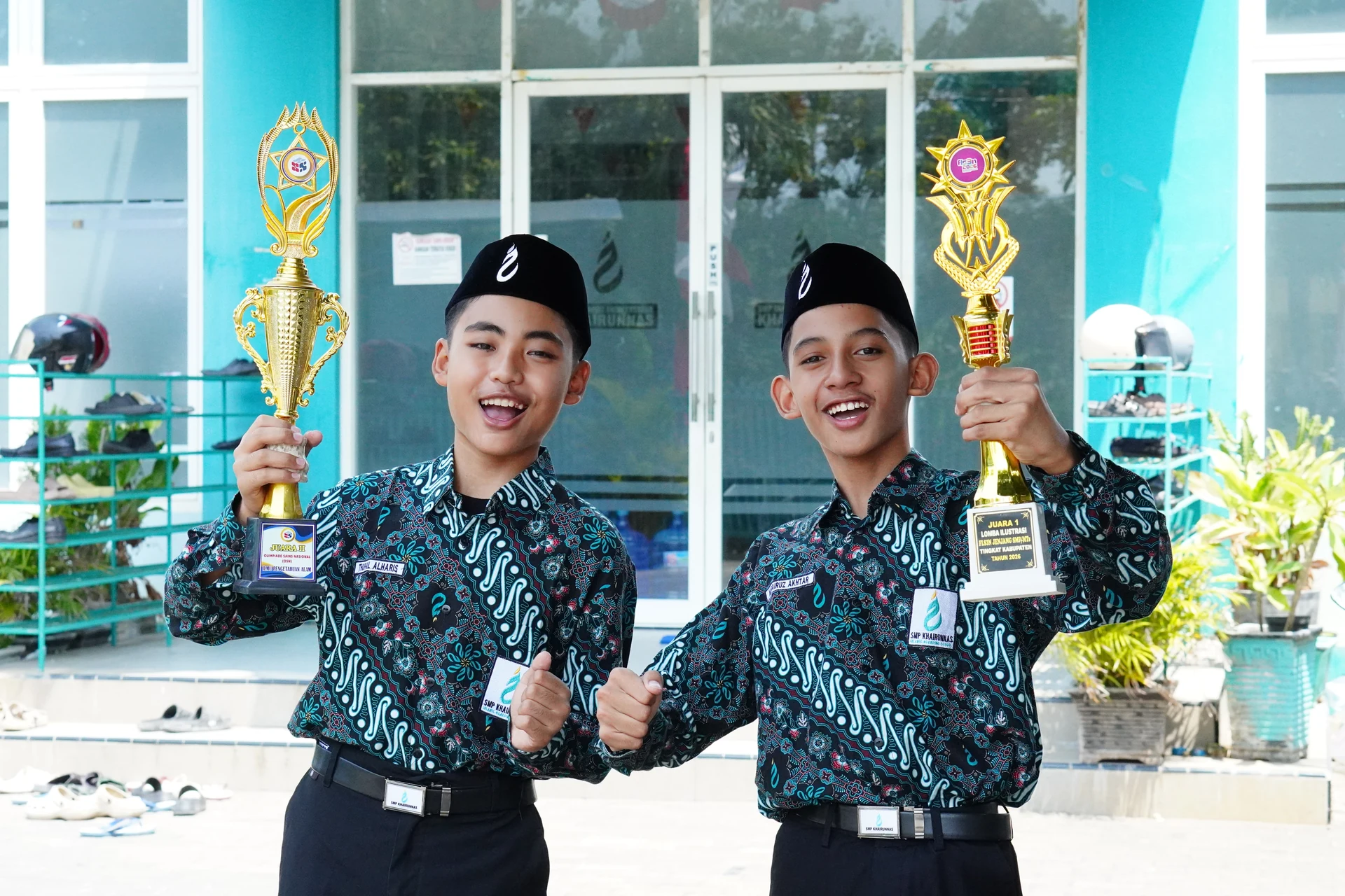 Dua santri putra mengangkat piala di depan gedung sekolah.